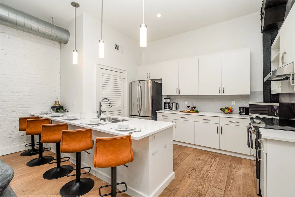 A sleek, stylish kitchen featuring a spacious island with barstools, pristine white cabinetry, and stainless steel appliances. The layout invites interaction, perfect for casual dining or mingling while preparing snacks and drinks.