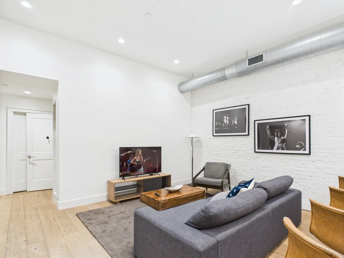 A cozy living room setup with a comfortable sofa, a wooden coffee table, a TV displaying a live performance, and black-and-white music-themed photographs on the wall, capturing a sense of relaxation and social gathering.