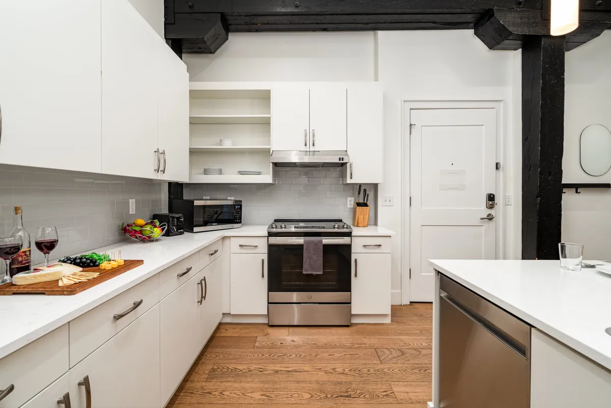 A modern kitchen scene featuring stainless steel appliances, a wooden countertop, and a spread of fresh fruits and cheese. The layout suggests a welcoming and versatile culinary space, ideal for cooking and entertaining.
