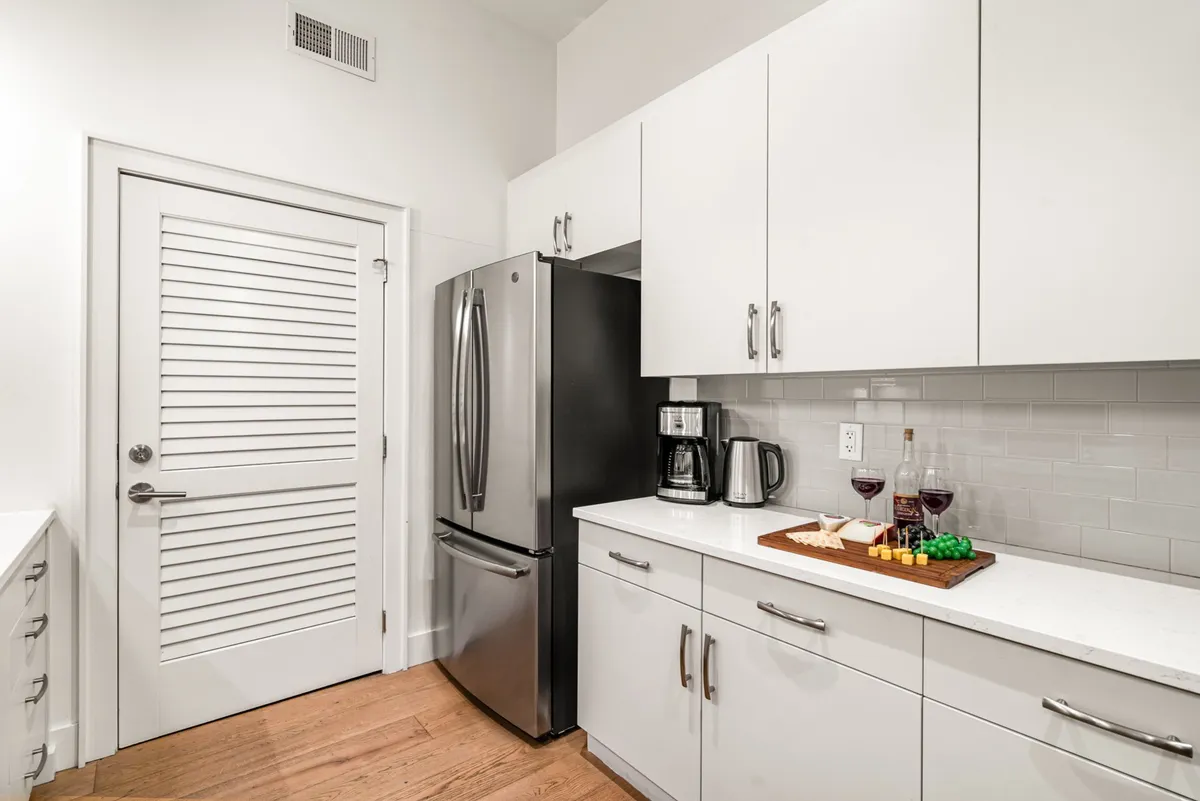 A cozy kitchen corner showcasing a stainless steel refrigerator, coffee maker, wine glasses, and a cheese platter. The setup suggests readiness for both breakfast and evening gatherings.