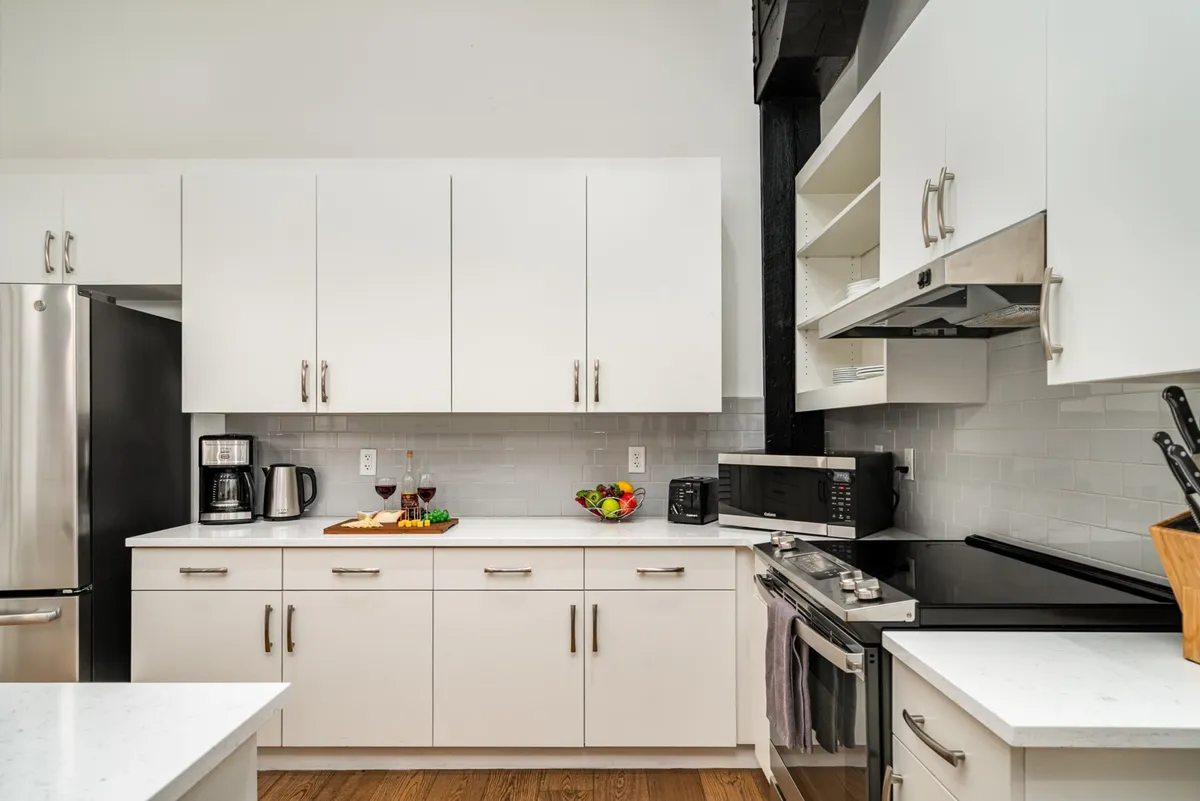 A bright, welcoming kitchen with white cabinetry, a countertop set with snacks and drinks, and up-to-date appliances. The arrangement encourages group gatherings and shared meal preparation.
