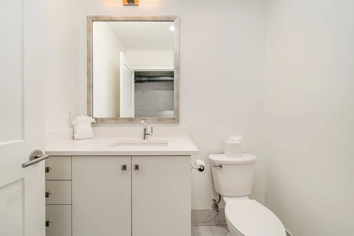 A serene half-bath with a minimalist design, showcasing a sleek mirror, an elegant sink, and a toilet. The space feels calm and clean—ideal for quick refreshes or extra flexibility for groups.