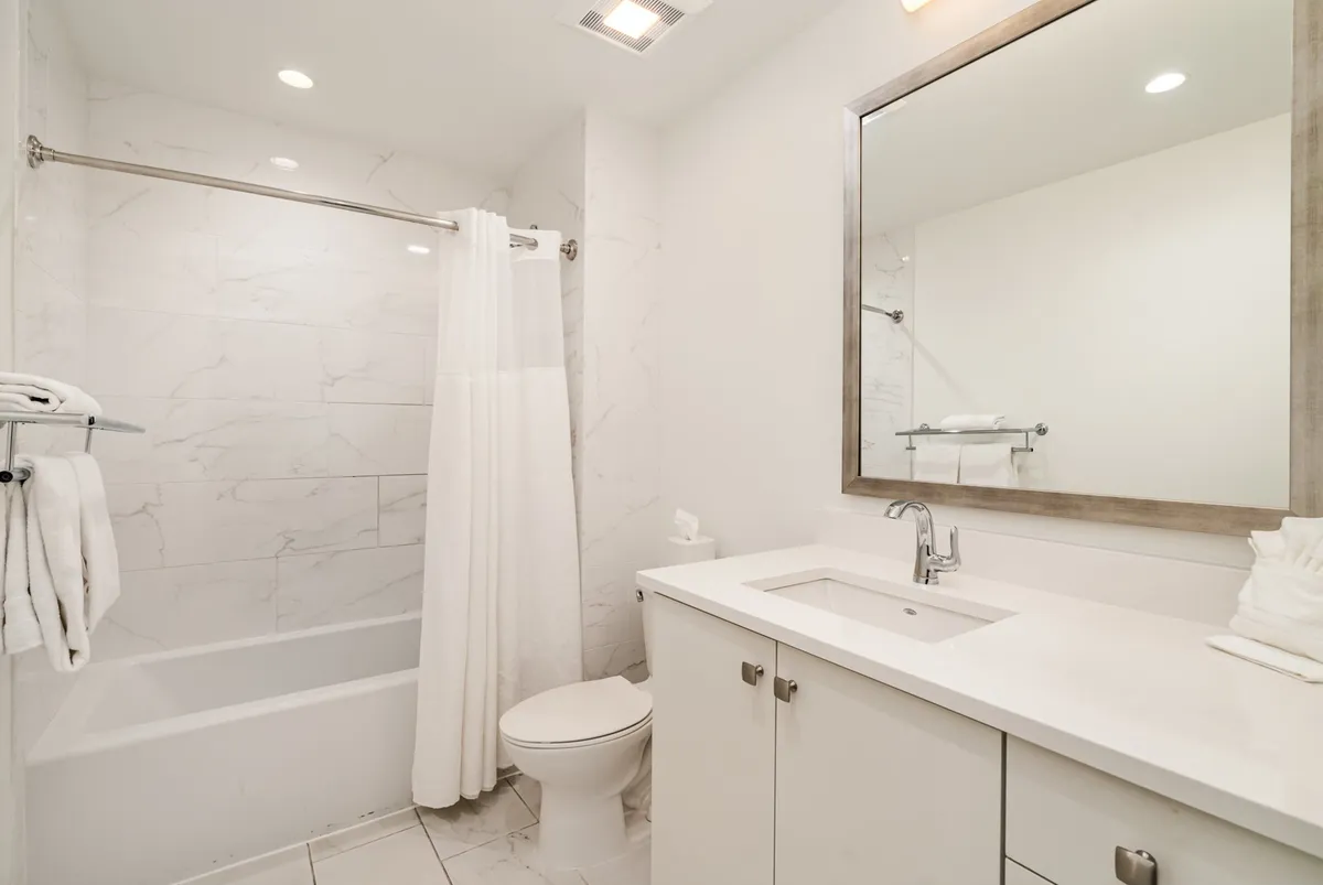 A tranquil, modern bathroom featuring a shower/tub combination, a large mirror above a spacious sink, and a toilet. The room is bright and inviting, with soothing tones that emphasize relaxation and cleanliness.